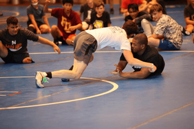 Teen wrestler grappling with an assistant coach at camp.