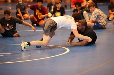 Teen wrestler grappling with an assistant coach at camp.