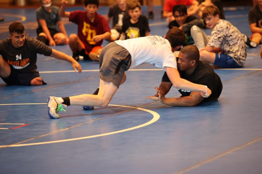 Teen wrestler grappling with an assistant coach at camp. 