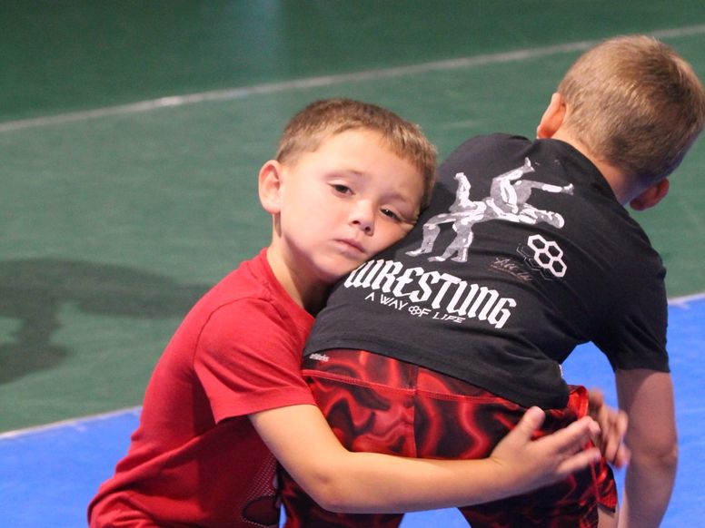 Two young boys in a tie-up at Ken Chertow's kids wrestling camp, one looking toward the camera