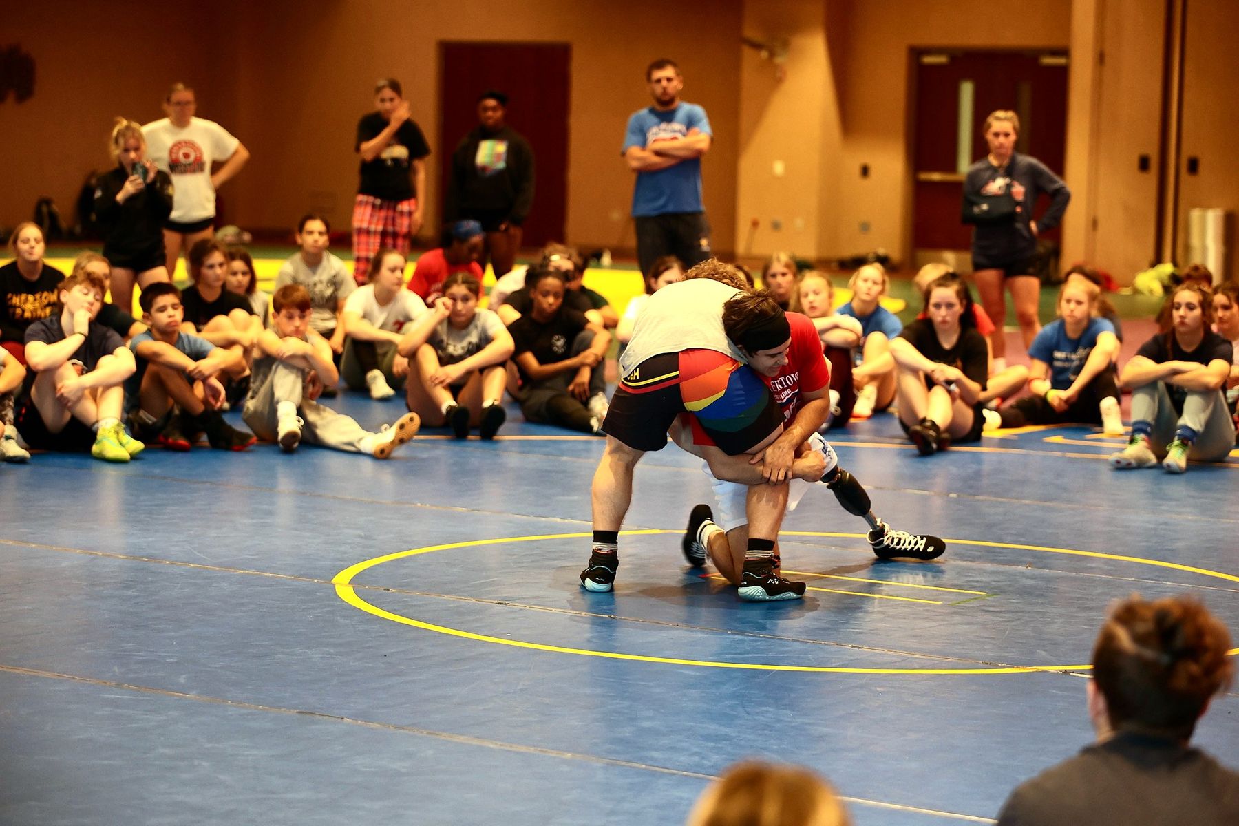 The whole camp seated around the mat watching a technique demonstration at summer wrestling camp