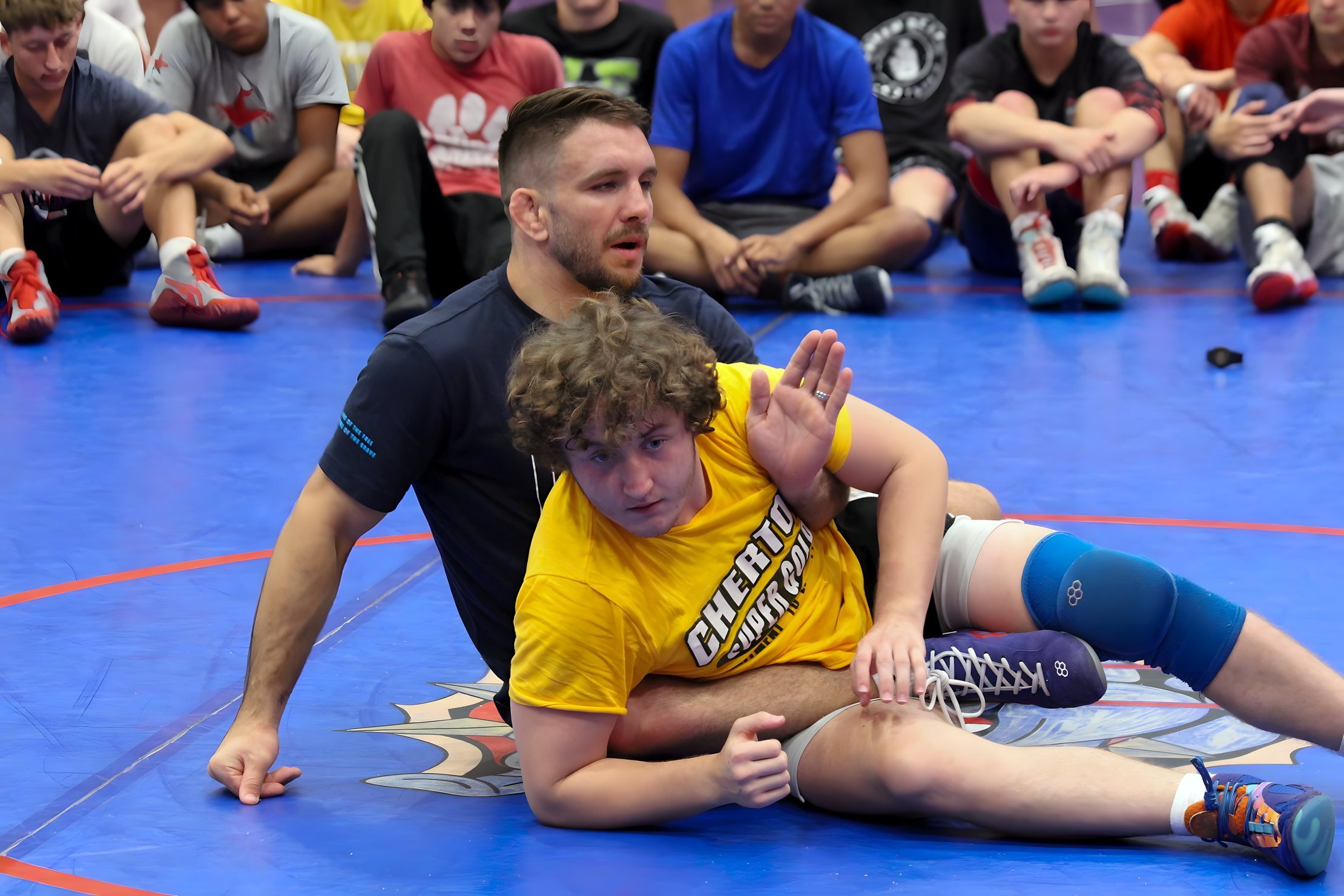 Zain Retherford demonstrating a move on a camper in a yellow Chertow shirt at summer wrestling camp