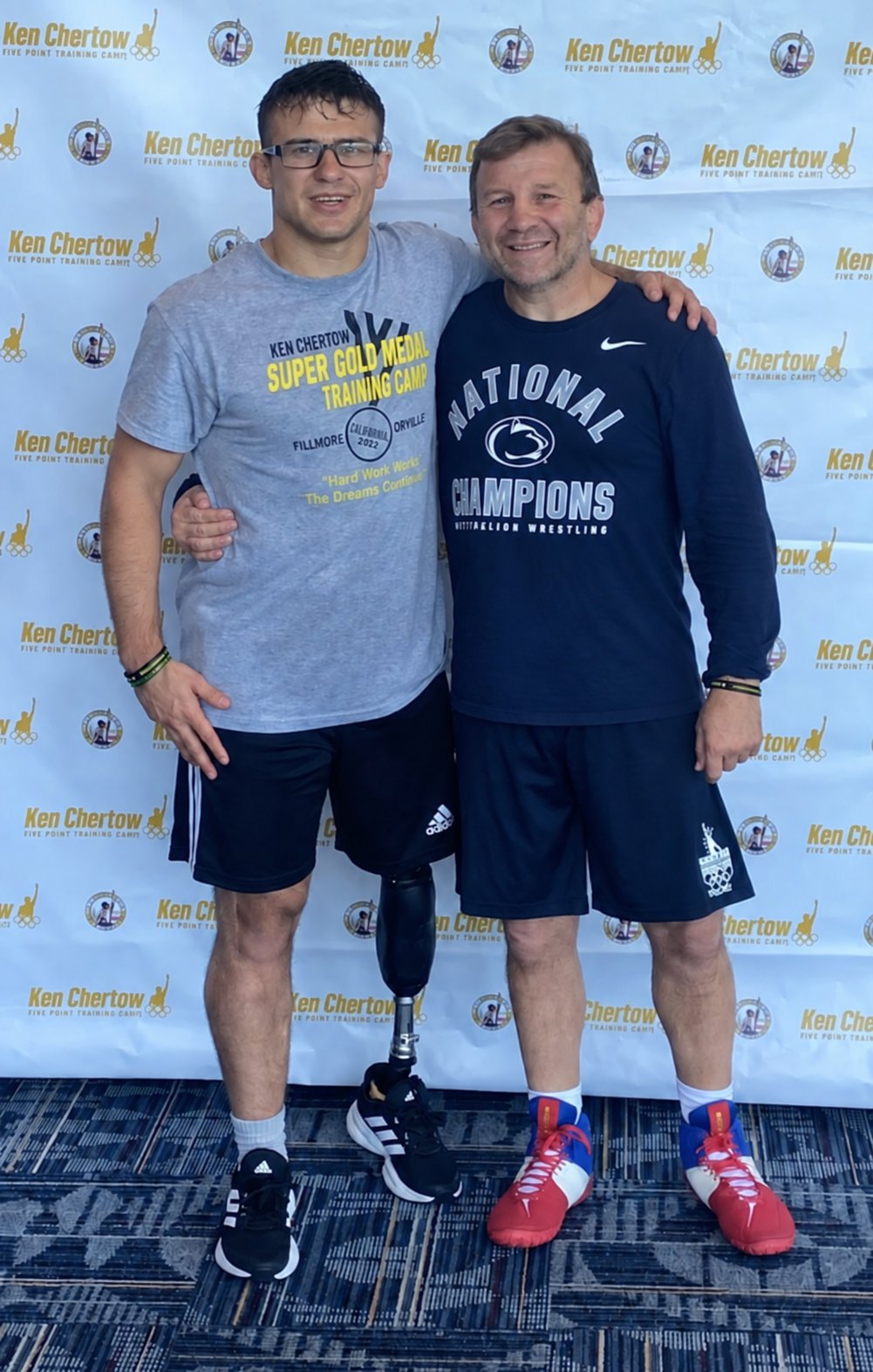 Doyle Trout and Coach Ken Chertow standing together in front of a camp backdrop.