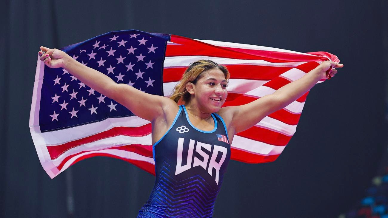 Taina Fernandez in a Team USA singlet, smiling as she runs with the American flag stretched out behind her in both hands