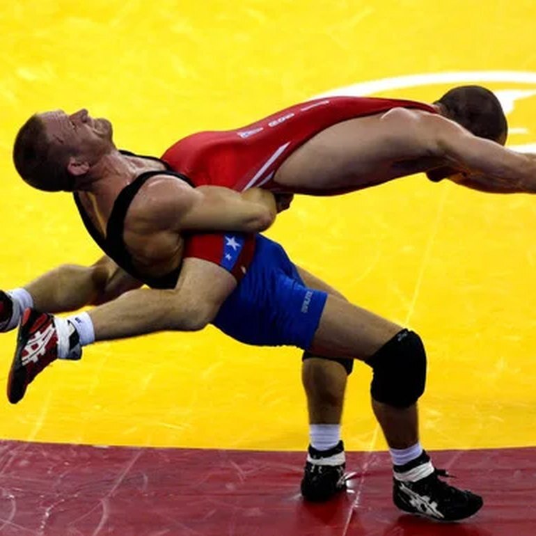 Dennis Hall mid-throw in a Greco-Roman match on a yellow mat, Ken Chertow wrestling camp coach