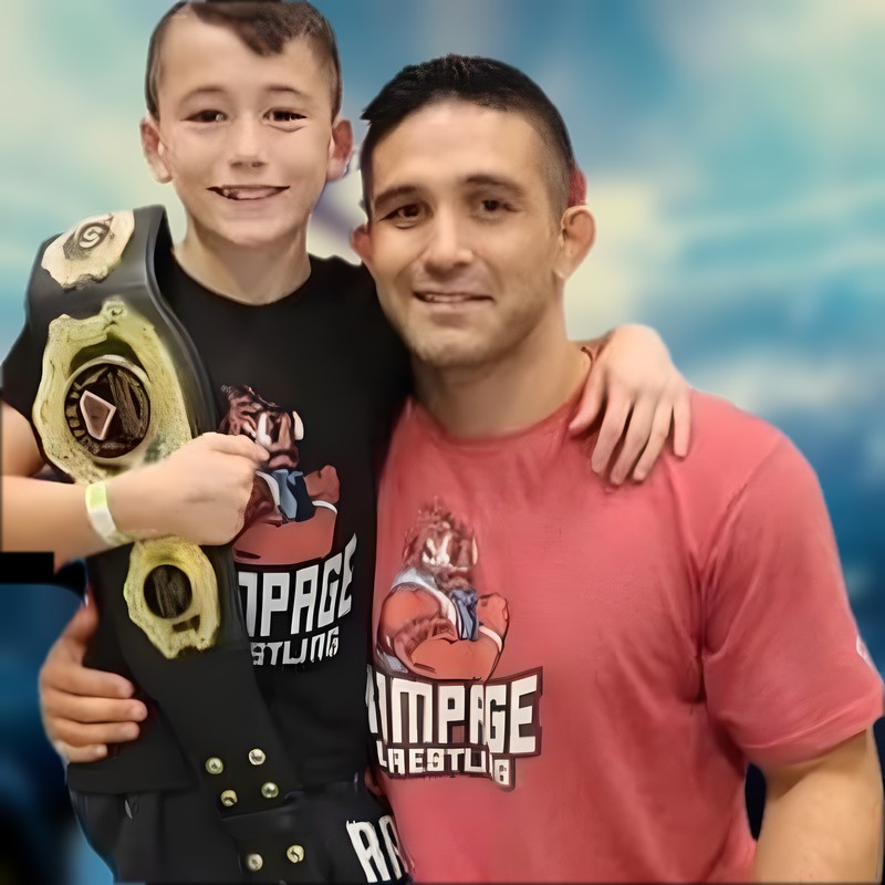 Jason Kiessling with his son Korbin, who is holding a championship belt, a Ken Chertow summer wrestling camp clinician