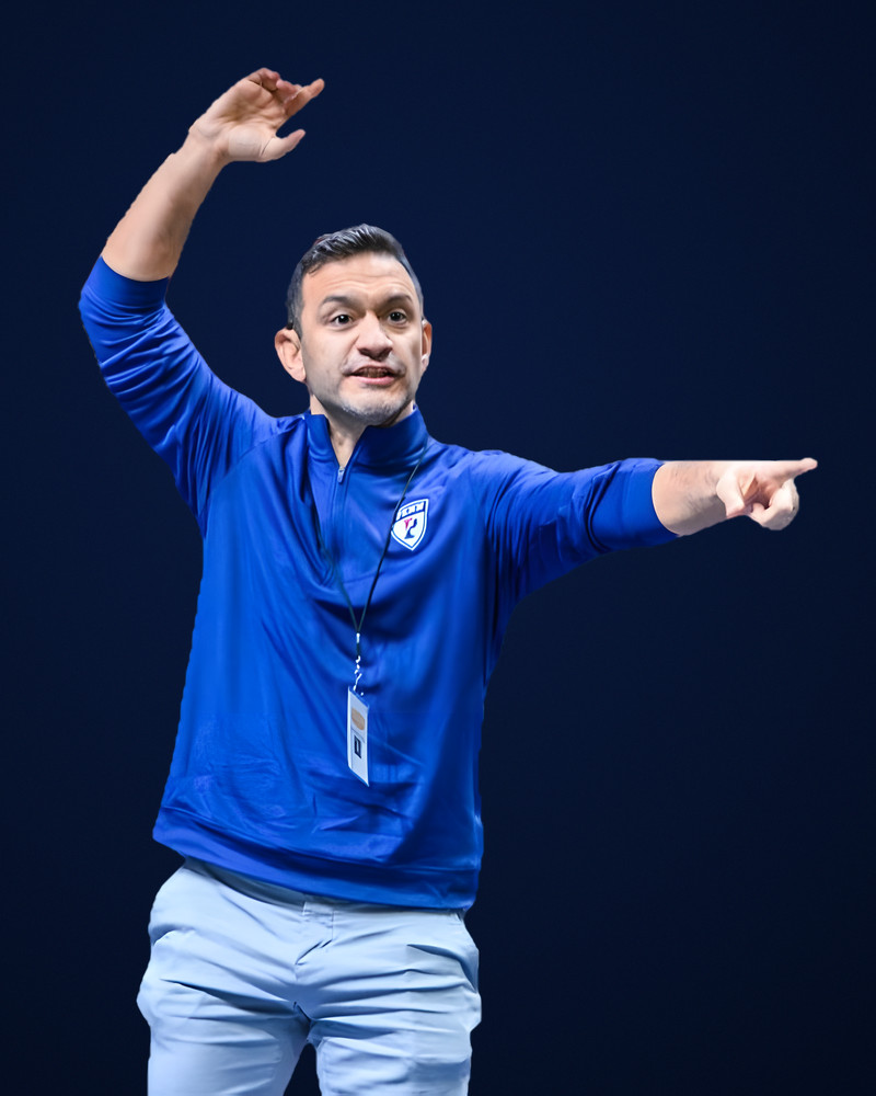 Matt Valenti in a Penn quarter-zip, one hand raised and pointing, Ken Chertow wrestling camp coach