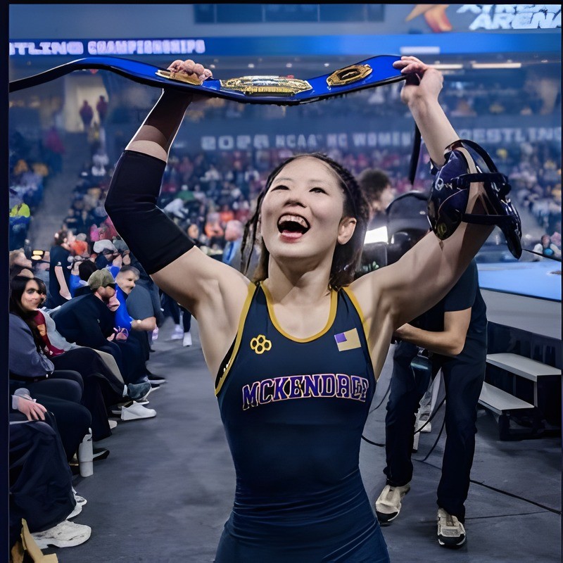 Yu Sakamoto holding a championship belt over her head at the 2026 NCAA championships, Ken Chertow wrestling camp coach
