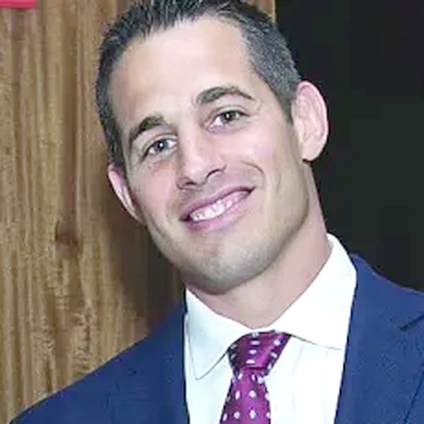 Jeff Zannetti smiling in a navy suit and purple tie, Ken Chertow wrestling camp staff member