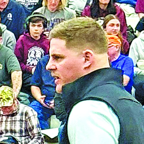 Tye Boyer in a dark vest, talking with a wrestler in headgear on the mat, on the staff at Ken Chertow's summer wrestling camp