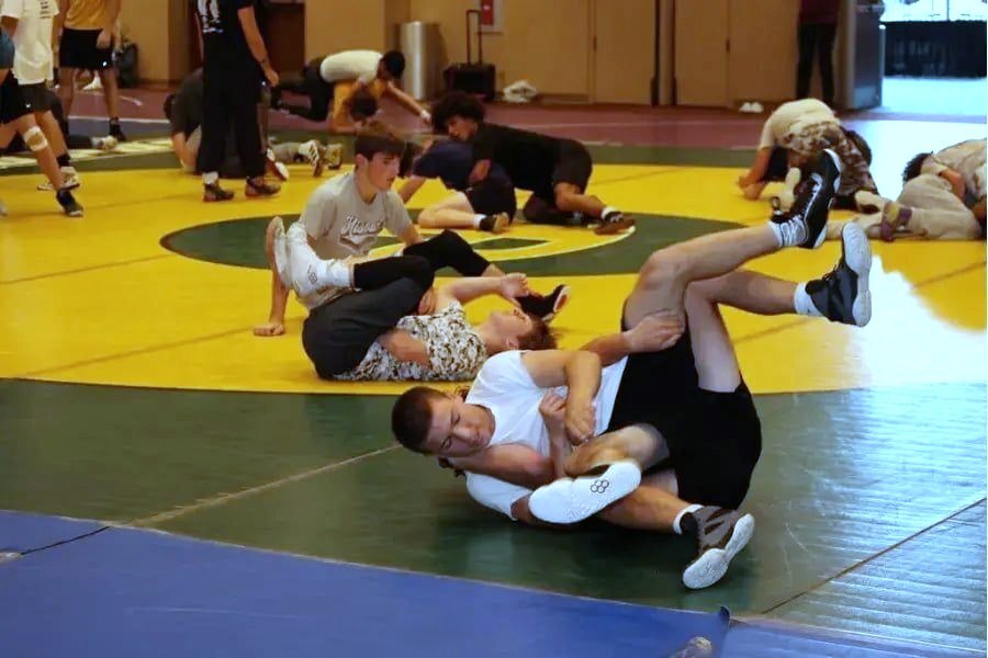 Middle school campers drilling moves in pairs on the yellow and green mat at summer wrestling camp