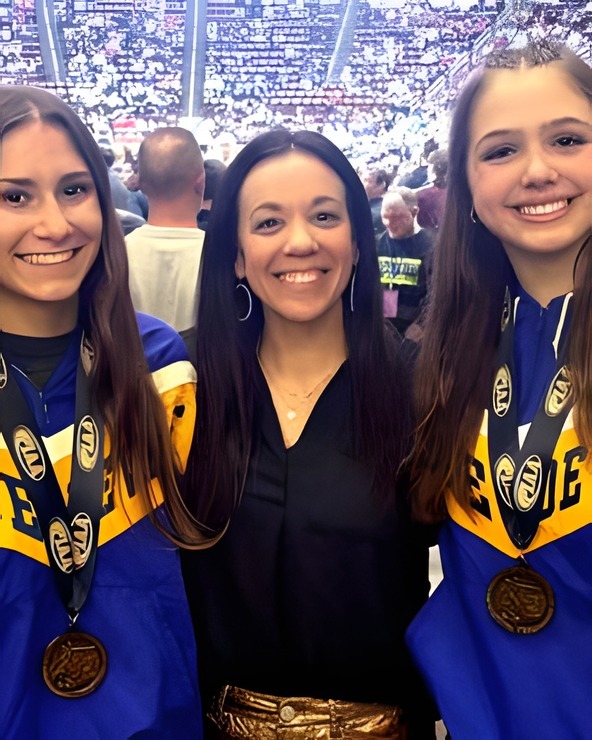 Amanda Lebec smiling with three of her medal-winning wrestlers, a packed arena behind them