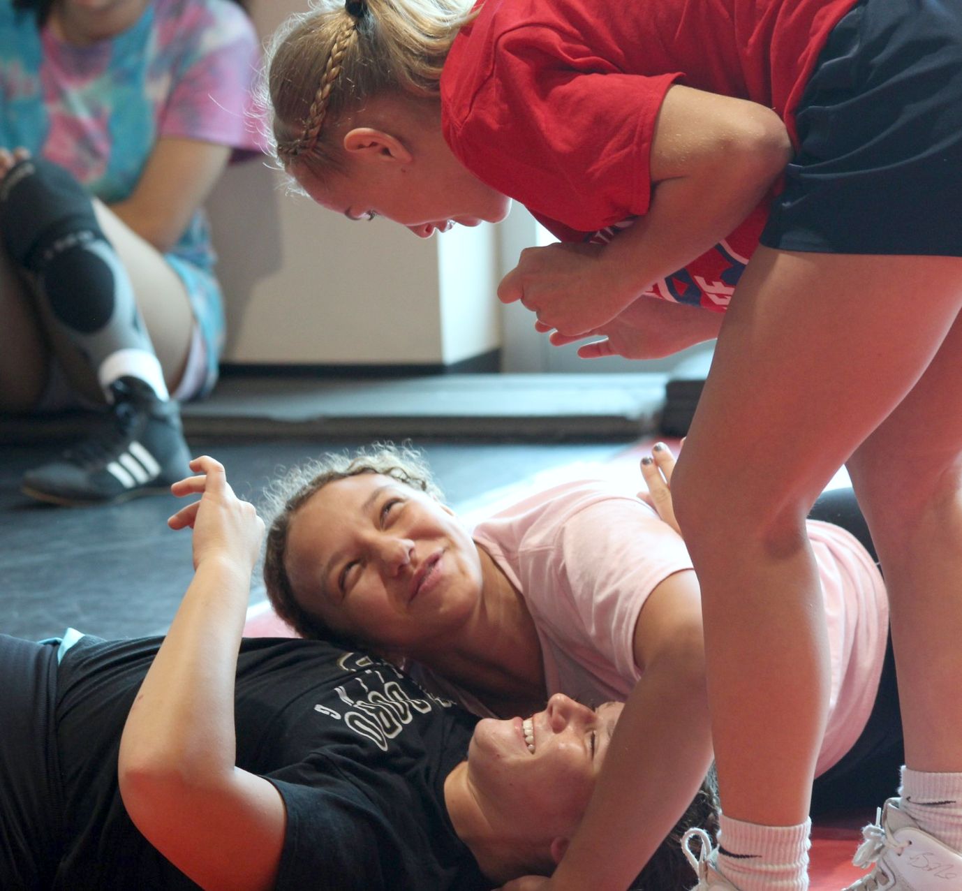 Three girls laughing on the mat during a technique demonstration at summer wrestling camp